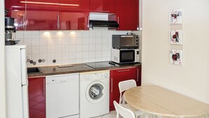 A compact kitchen with red cabinets, a microwave, a toaster, a dishwasher, and a washing machine. - Apartment with a view of the garden and an unobstructed view of the ocean! (Le Pradet)