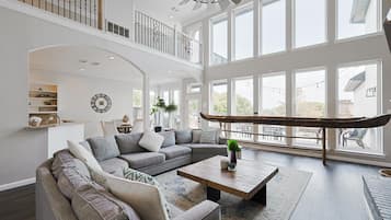 Un salon spacieux, doté d’un grand canapé d’angle, d’une table basse et offrant une vue sur l’extérieur grâce à de grandes fenêtres.