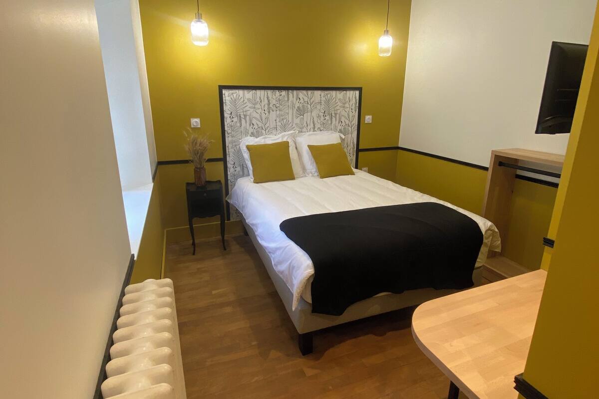 A bedroom with a bed, bedside tables, a radiator, and a desk with a chair.