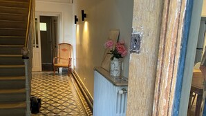 Un pasillo con suelo a cuadros, una escalera de madera, un radiador y una silla.