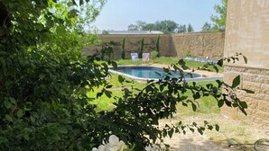 Un jardín con piscina, rodeado de vegetación y un muro de piedra.