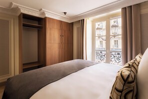 Ett hotellrum med en säng, en garderob och ett fönster med utsikt över byggnader.