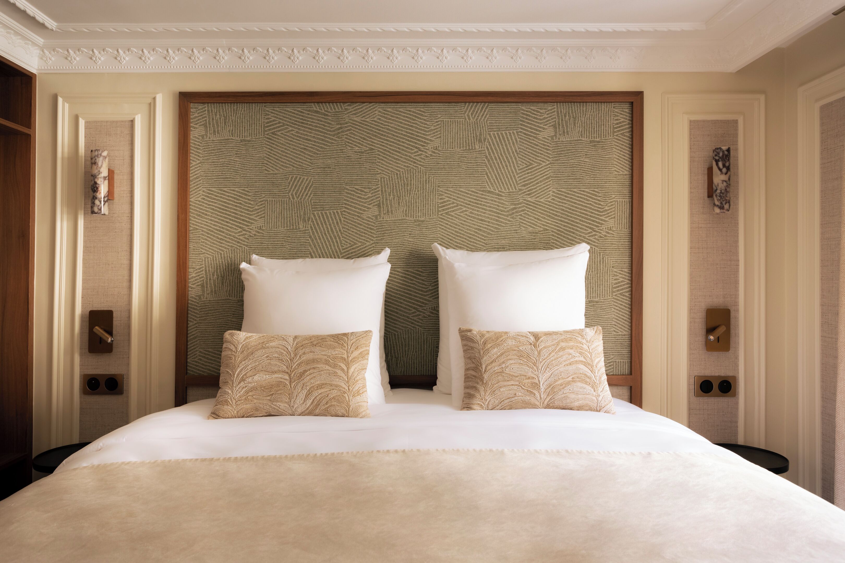 A hotel room with a large bed, two pillows, a headboard with a geometric pattern, and a wooden frame.
