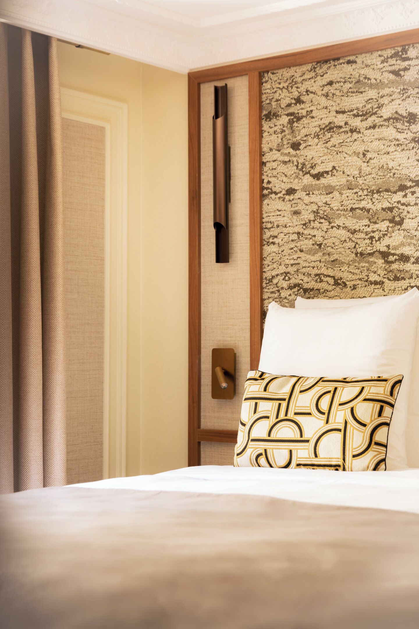 Een hotelkamer met een bed, een gestreept kussen, een houten hoofdbord, een deur en een gordijn.