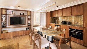 Una cocina moderna con armarios de madera, encimera de mármol, horno empotrado y comedor con una mesa grande y sillas.