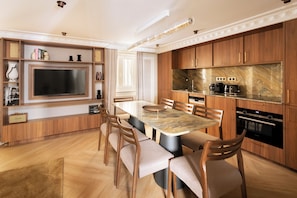 Een moderne keuken met houten kastjes, een marmeren aanrechtblad, een inbouwoven en een eethoek met een grote tafel en stoelen.