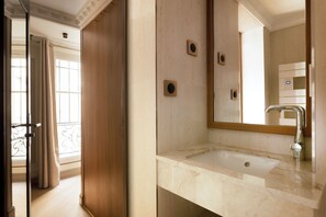 Un baño con lavamanos de mármol, un espejo y una puerta que da a otra habitación.