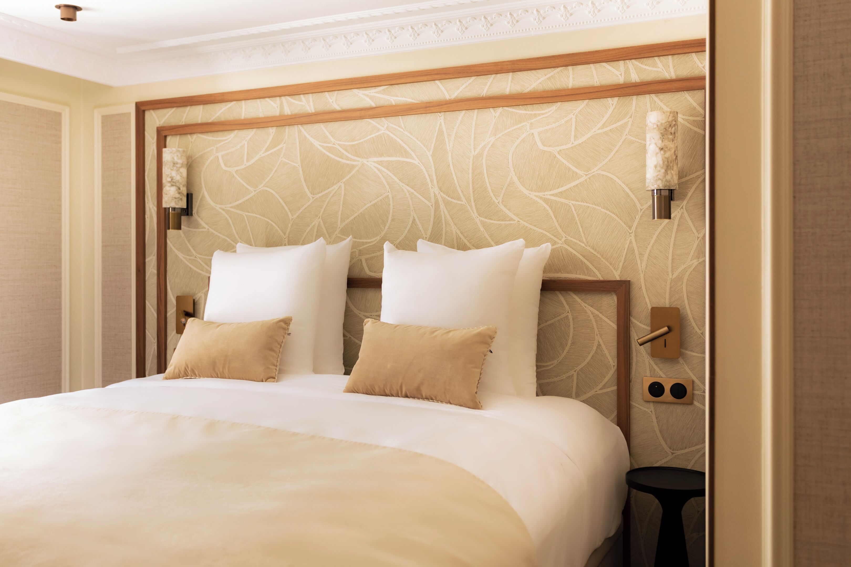 A hotel room with a large bed, two wall-mounted light fixtures, and a small side table.