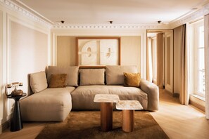 A living room with a sectional sofa, a small side table, and a framed artwork on the wall. - Merveil - Luxury Suite - Louvre - Rivoli (Paris)