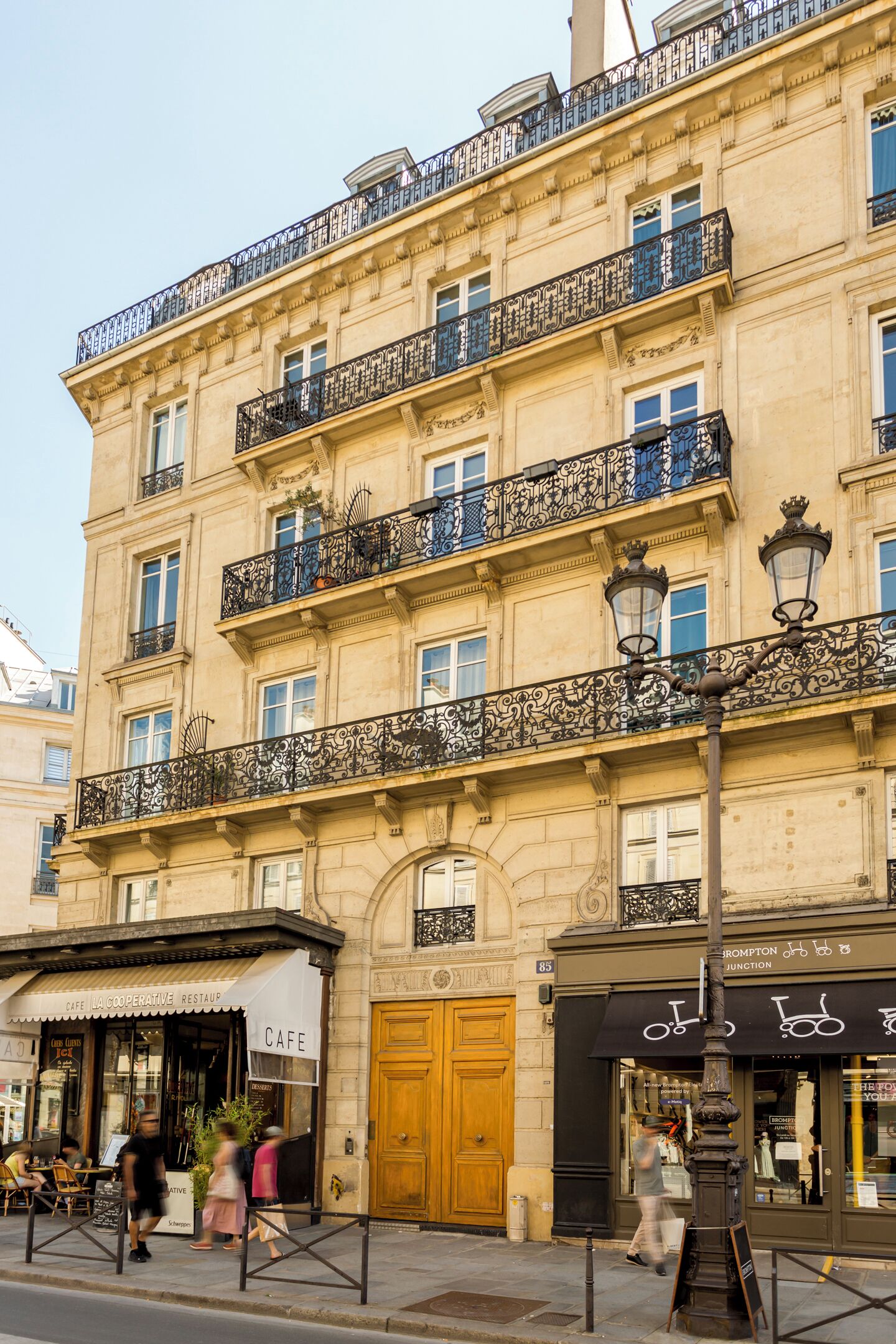 Un edificio de varios pisos con balcones ornamentales, una cafetería en la planta baja y una tienda de bicicletas al nivel de la calle.