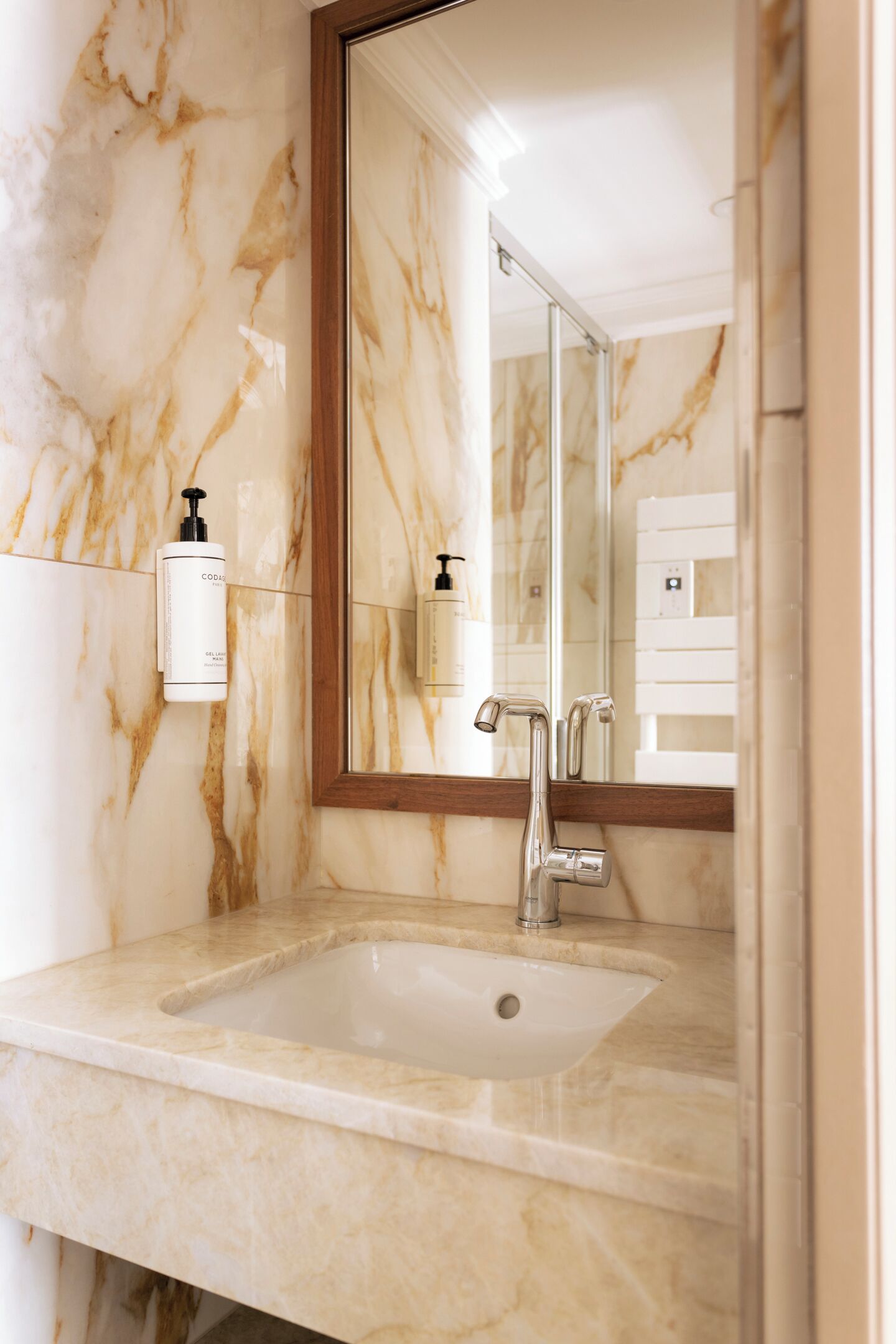 A bathroom with a marble sink, a mirror, and a hand soap dispenser.