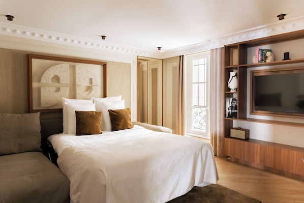 A well-lit hotel room with a large bed, a sofa, a TV, and a bookshelf.