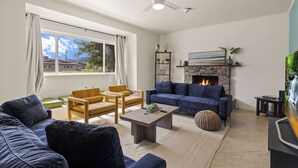 A living room with a fireplace, sofas, a coffee table, and a television. - Indio Poolside Retreat Getaway by Navigate Stays (Indio)