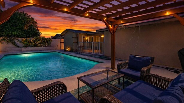 A pool area with a pergola, lounge chairs, and a small building with a balcony. - Indio Poolside Retreat Getaway by Navigate Stays (Indio)
