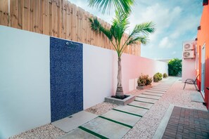 Un sendero estrecho con una pared de baldosas, una palmera y un edificio rojo con unidades de aire acondicionado.