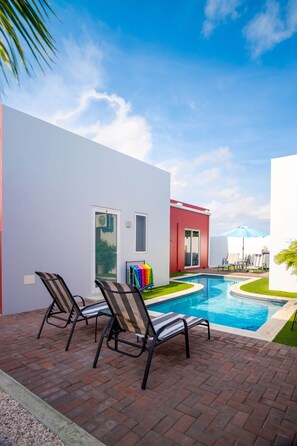A modern outdoor pool area with two lounge chairs, a red building, and a clear blue sky.