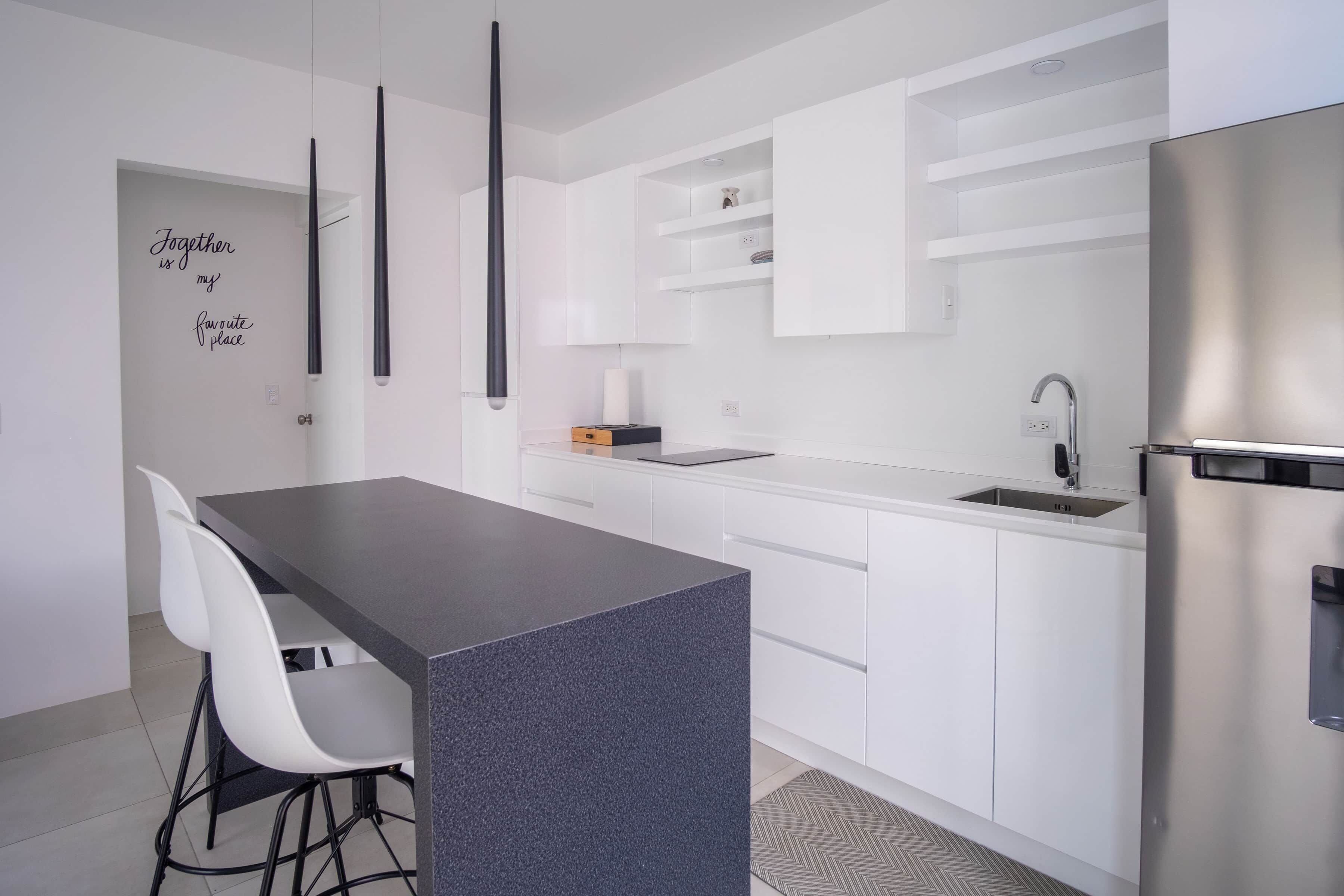 Eine moderne Küche mit weißen Schränken, einer dunklen Arbeitsplatte und einem Edelstahl-Kühlschrank.