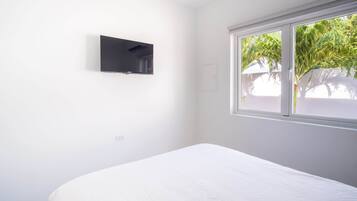 Una habitación con una cama, un televisor montado en la pared y un ventanal con vistas al verdor.