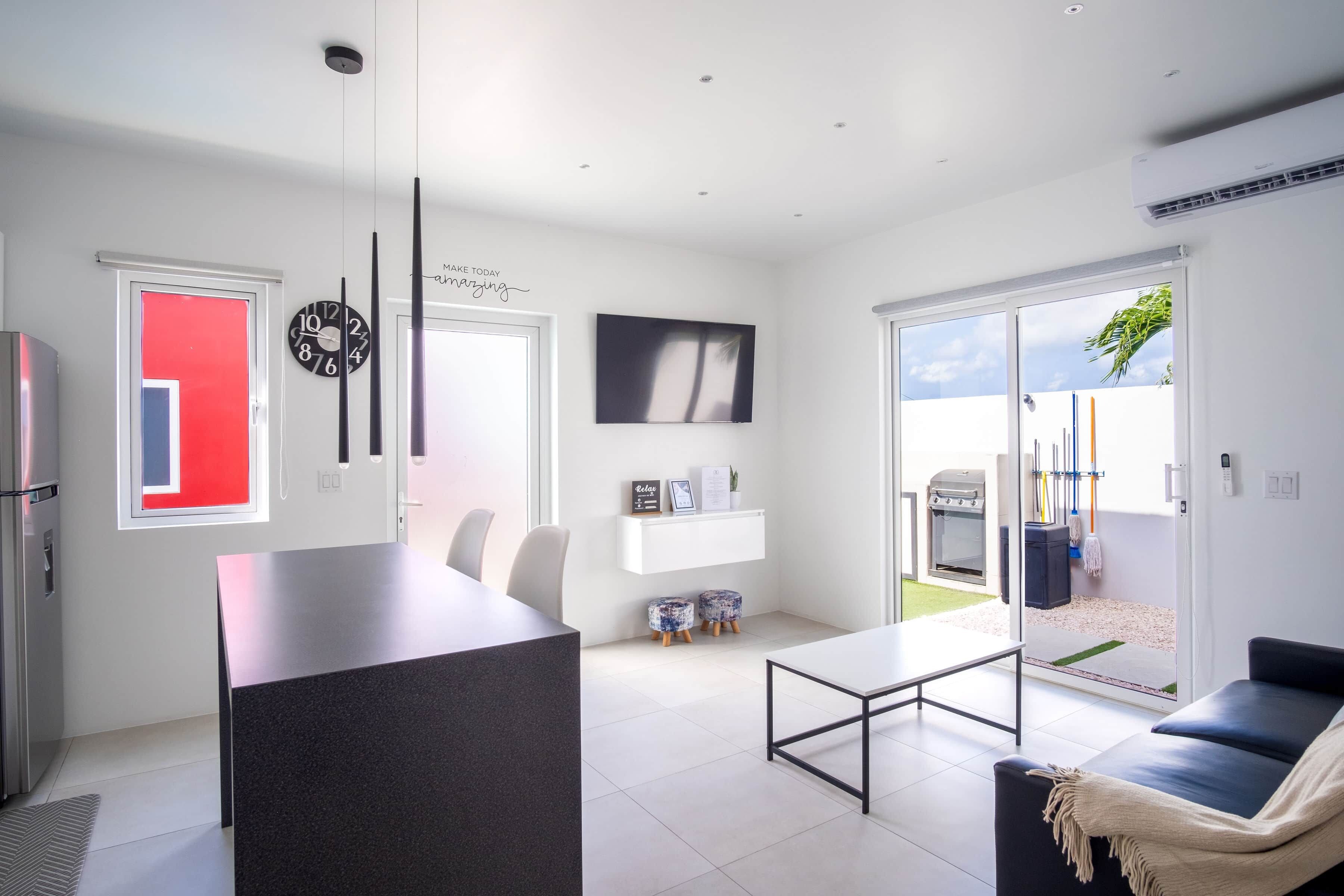Eine moderne Küche mit Kochinsel, ein Essbereich mit schwarzem Tisch und eine Wohnbereich mit Sofa und Fernseher.