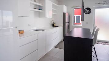 Una cocina moderna con armarios blancos, una isla con encimera negra y un refrigerador de acero inoxidable.