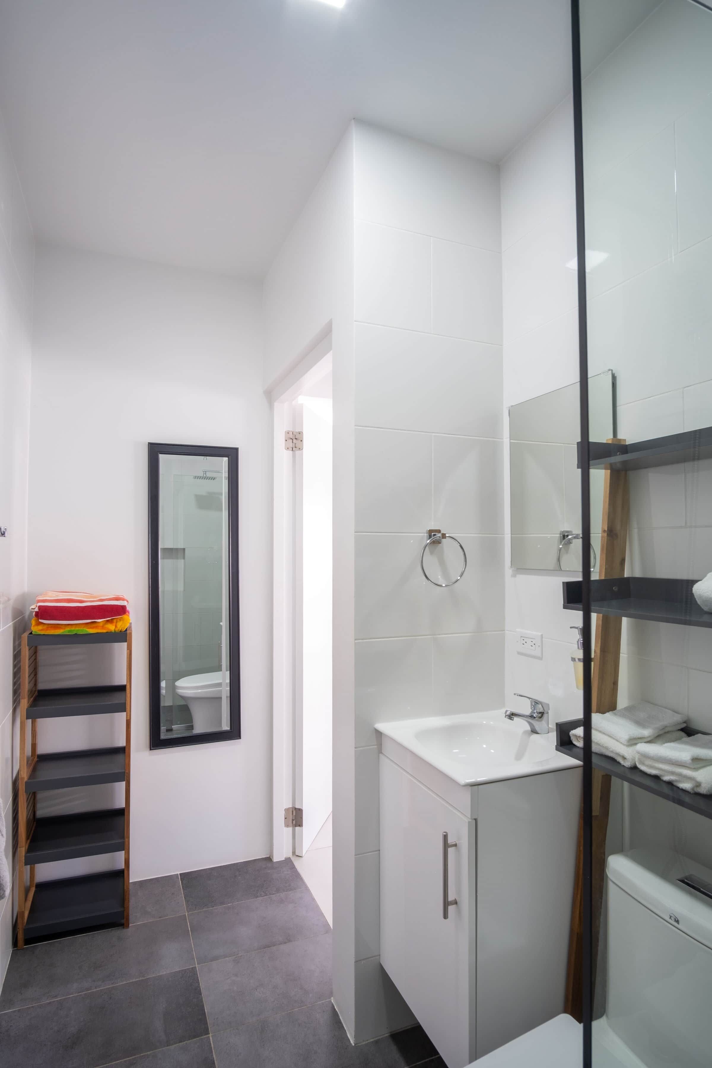 Un bagno moderno con cabina doccia in vetro, un lavandino bianco e uno specchio.