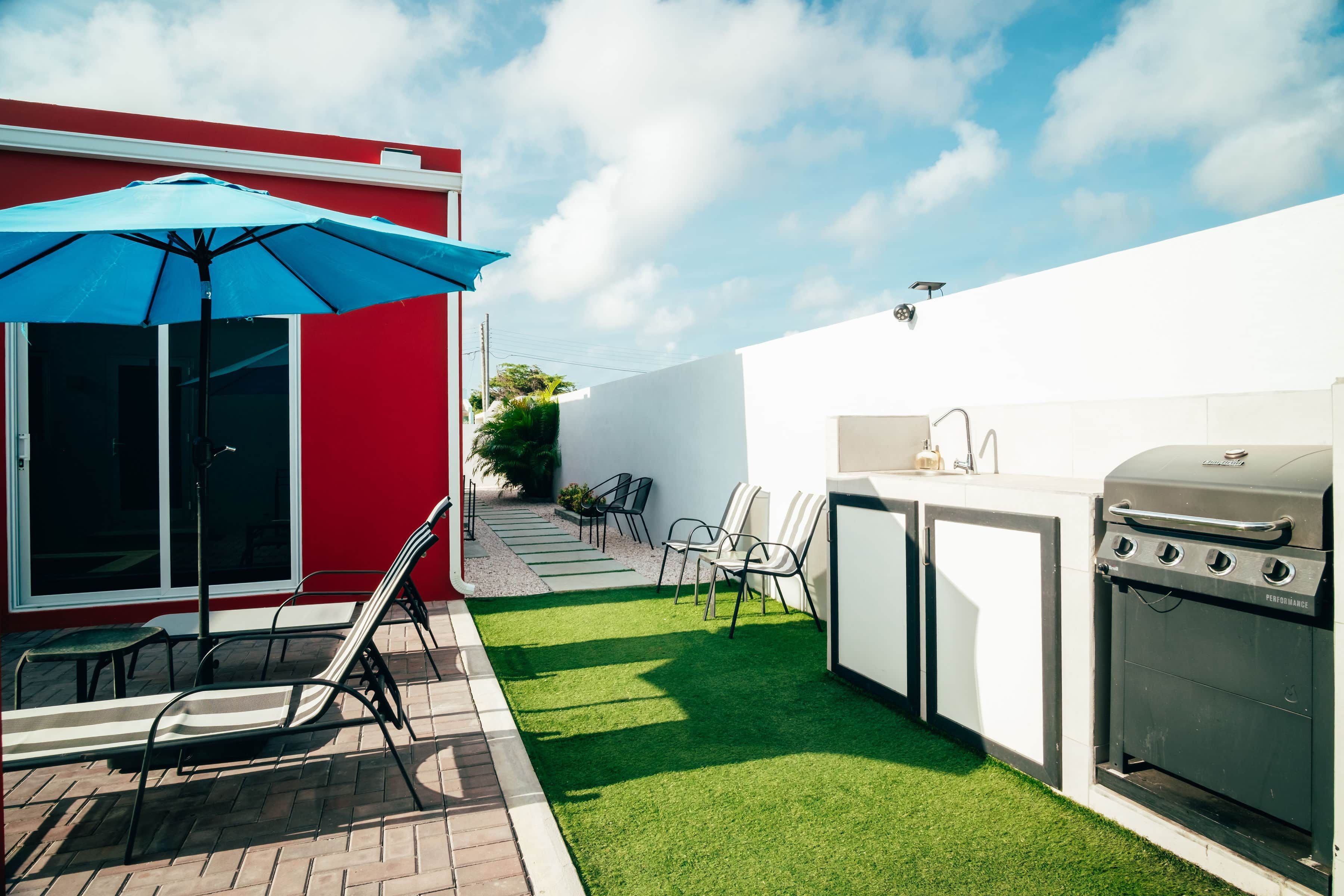 Eine Terrasse mit Grill, Stühlen und Sonnenschirm.