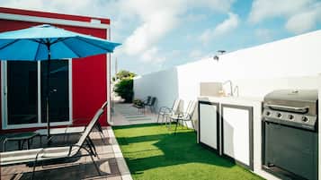 Eine Terrasse mit Grill, Stühlen und Sonnenschirm.