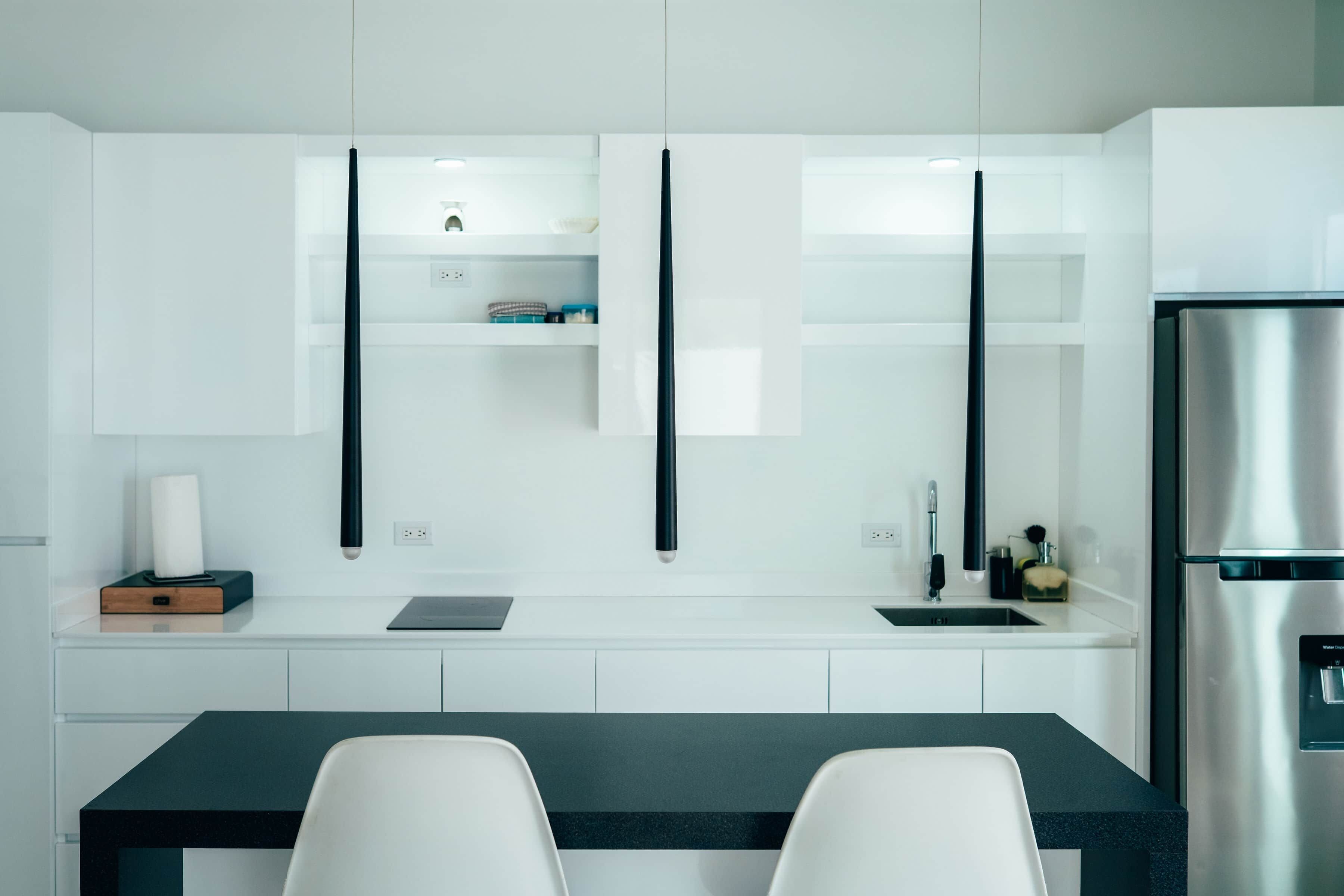 Une cuisine moderne avec des meubles blancs, un réfrigérateur en acier inoxydable et un plan de travail noir.
