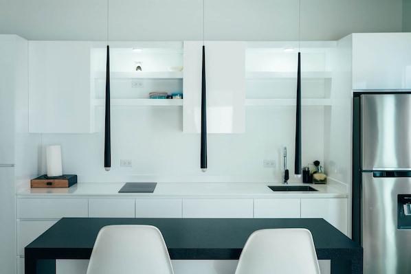 Une cuisine moderne avec des meubles blancs, un réfrigérateur en acier inoxydable et un plan de travail noir.