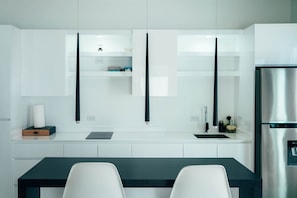 Une cuisine moderne avec des meubles blancs, un réfrigérateur en acier inoxydable et un plan de travail noir.
