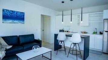 Un salon moderne comprenant un canapé, une table basse et un coin cuisine avec un comptoir-bar et des tabourets.
