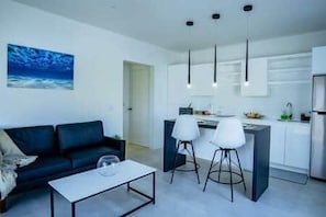 Un salon moderne comprenant un canapé, une table basse et un coin cuisine avec un comptoir-bar et des tabourets.