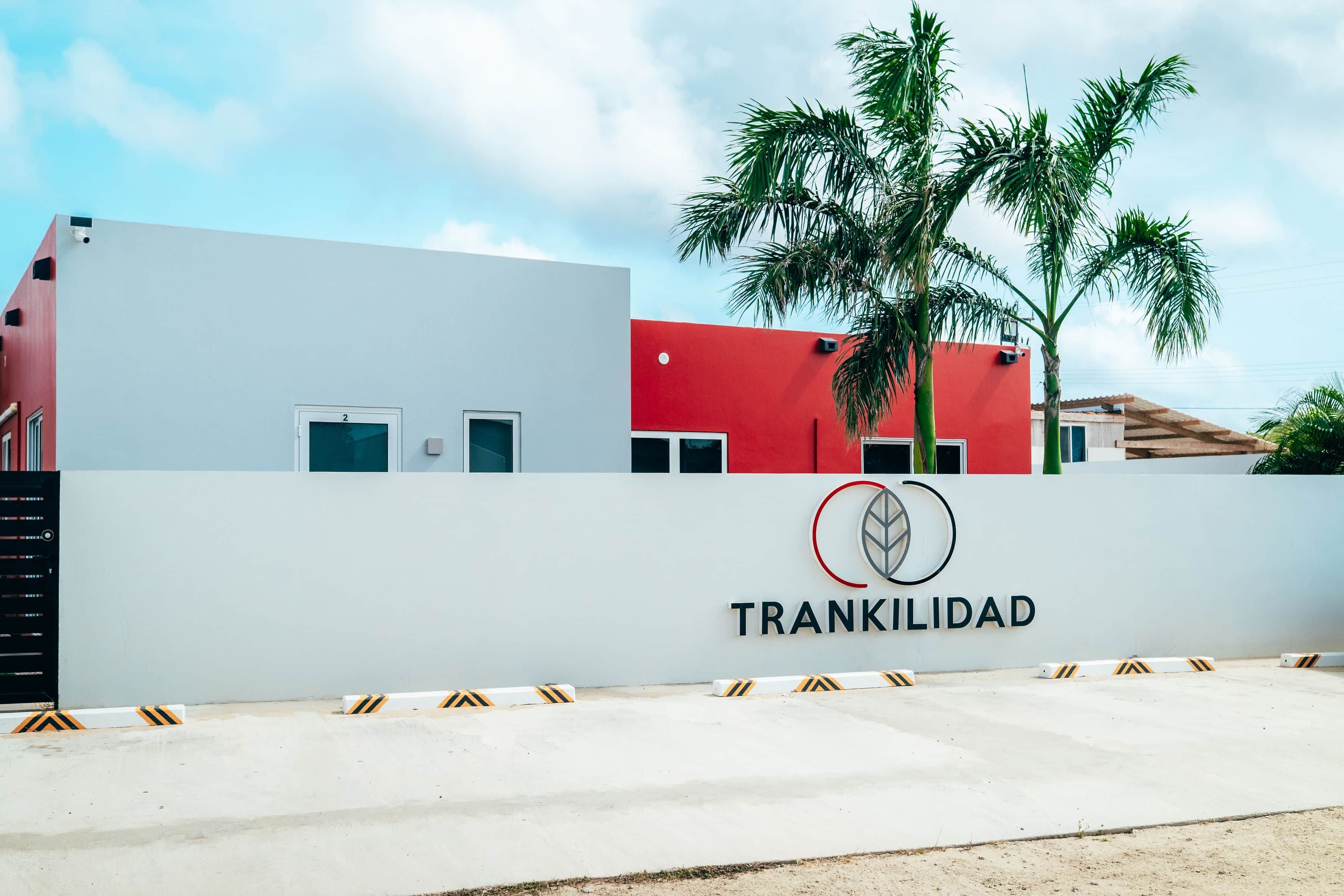 Ein Gebäude mit weißer und roter Fassade, eine Palme und ein Schild mit dem Schriftzug 'TRANKILIDAD'.