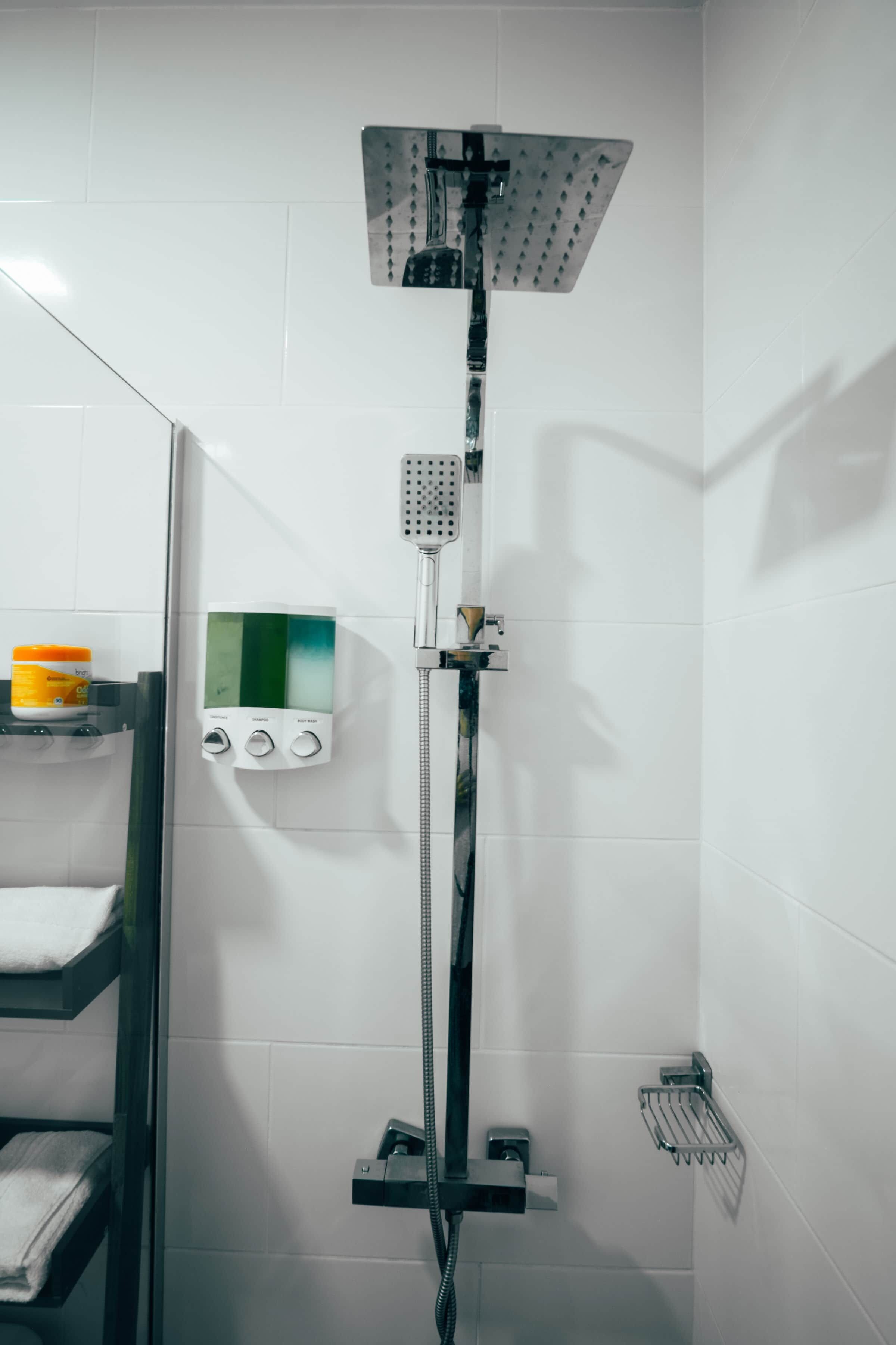 A shower with a handheld showerhead and a fixed showerhead, a control panel with three buttons, and a towel rack with a towel.