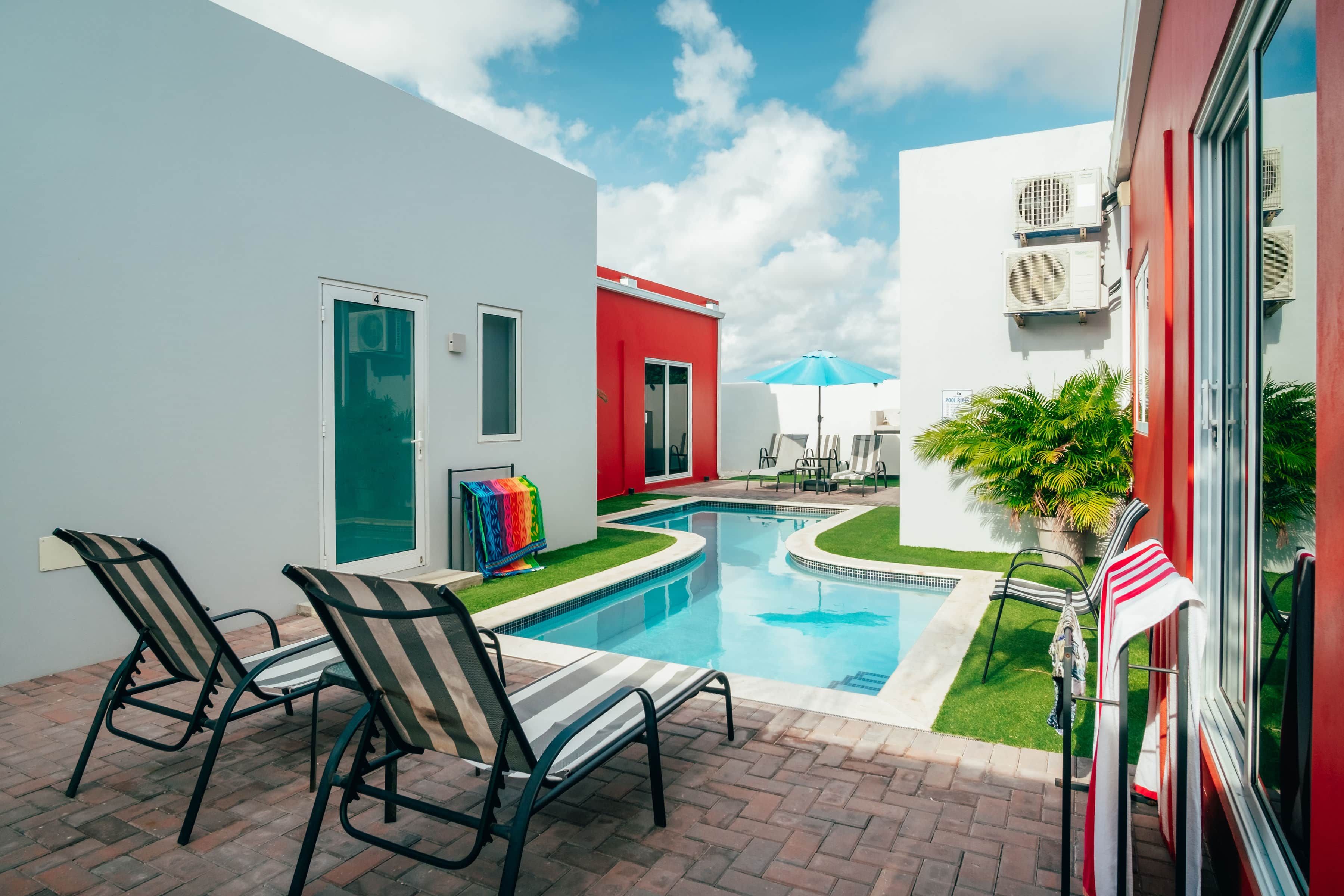 Une piscine avec des chaises longues, une porte et un bâtiment rouge.