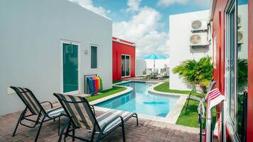 Une piscine avec des chaises longues, une porte et un bâtiment rouge.
