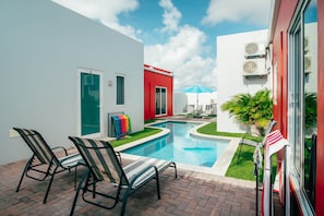 Une piscine avec des chaises longues, une porte et un bâtiment rouge.