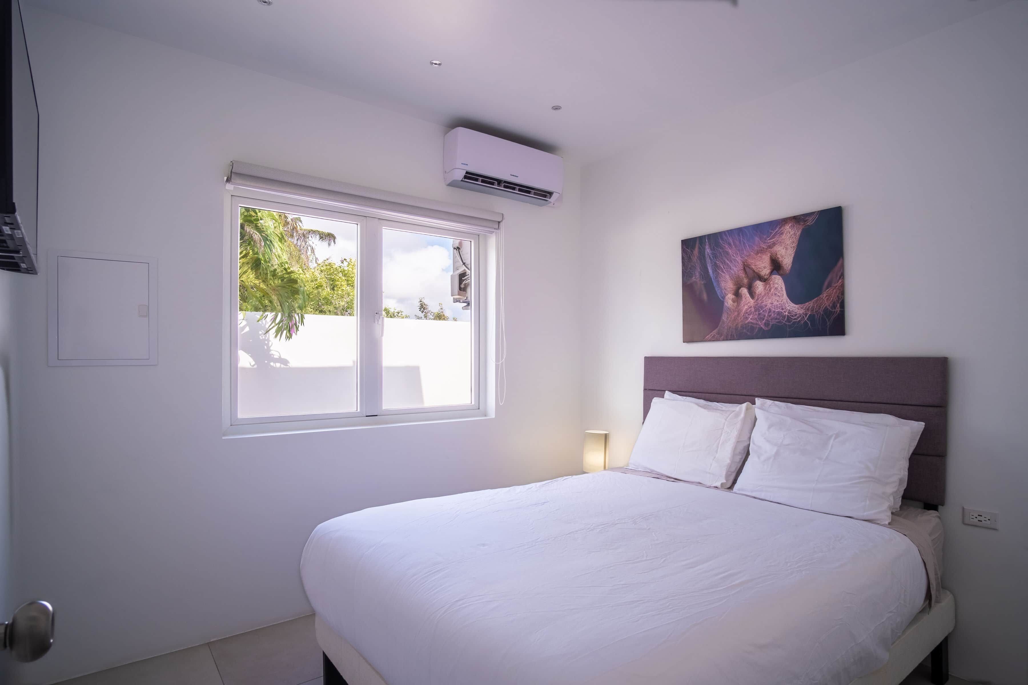 Ein Hotelzimmer mit Bett, Fenster, Klimaanlage, einem Wandbild und einer Nachttischlampe.