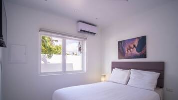 Ein Hotelzimmer mit Bett, Fenster, Klimaanlage, einem Wandbild und einer Nachttischlampe.