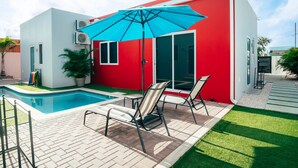 Ein modernes Haus mit rotem Anstrich, einem Schwimmbad und einer Terrasse mit Stühlen und Sonnenschirm.