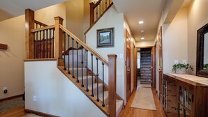 A wooden staircase with black balusters leading to a landing, a hallway with a wooden cabinet and a mirror, and a framed picture on the wall. - RA410 | Excellent Amenities | Winter Shuttle | Pool | Hot Tub | Views (Steamboat Springs)