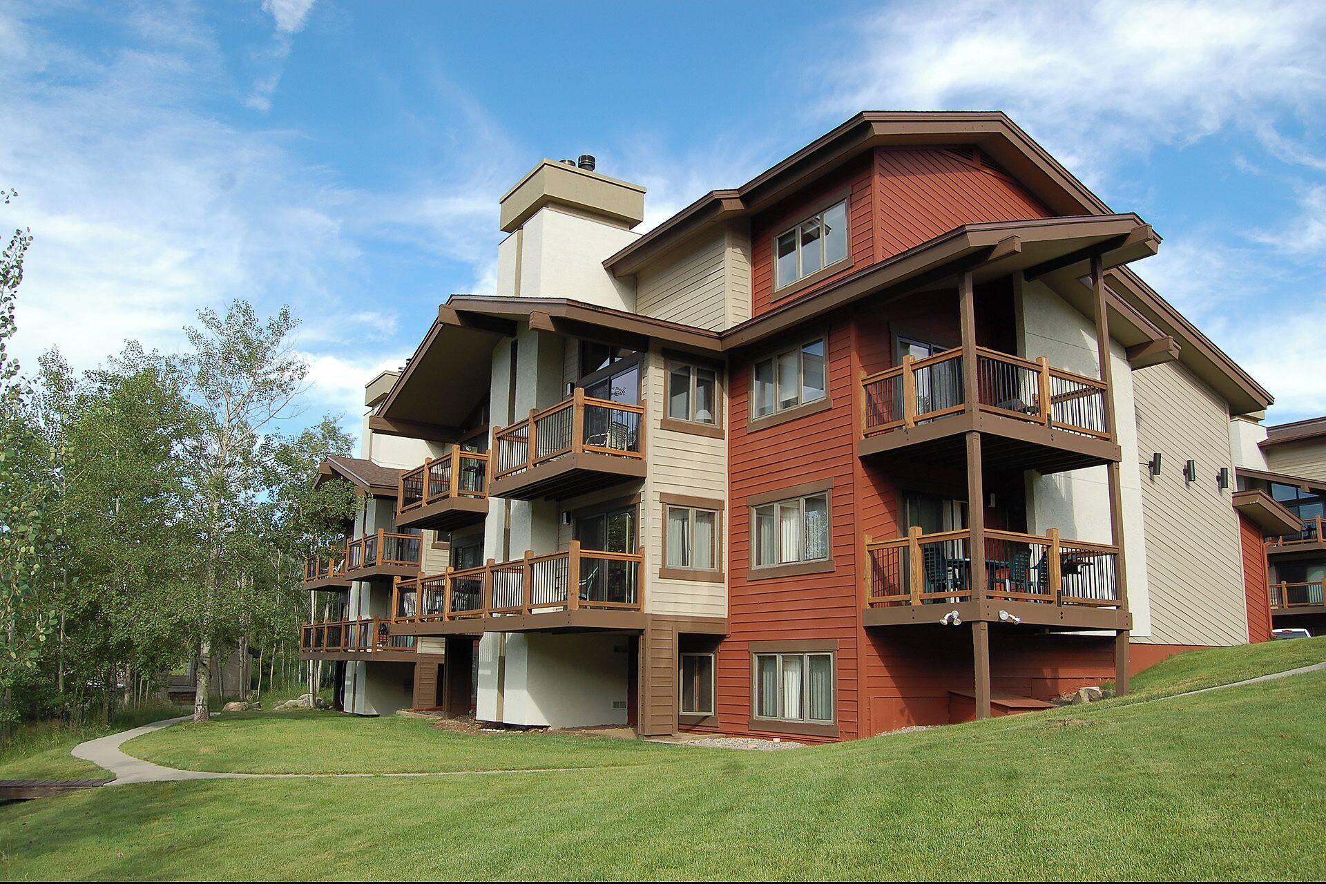 A multi-story building with balconies, a pathway, and a grassy area.