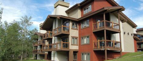 A multi-story building with balconies, a pathway, and a grassy area.