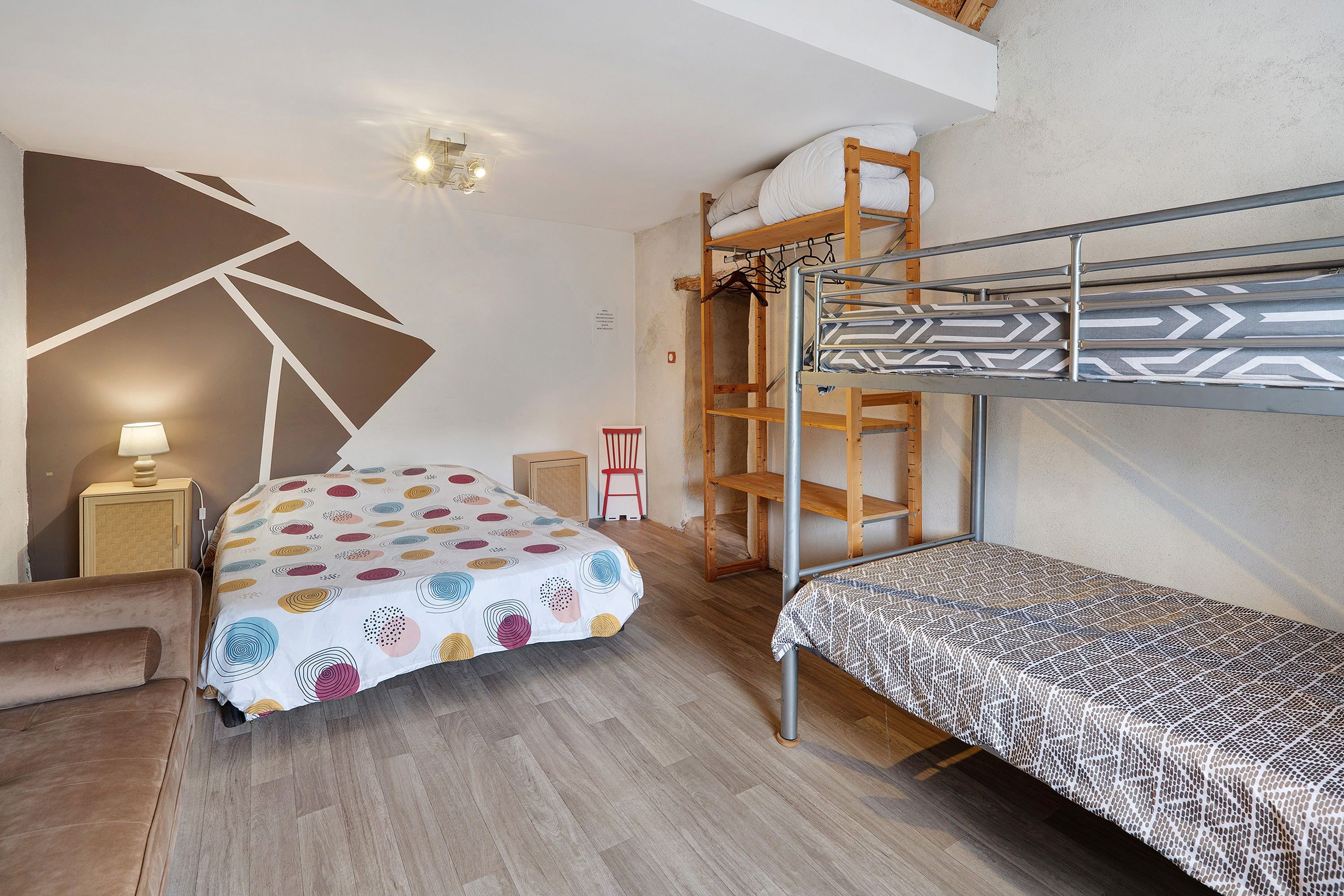 Une pièce de taille modeste comprenant un lit superposé, un lit simple, un bureau et une chaise.