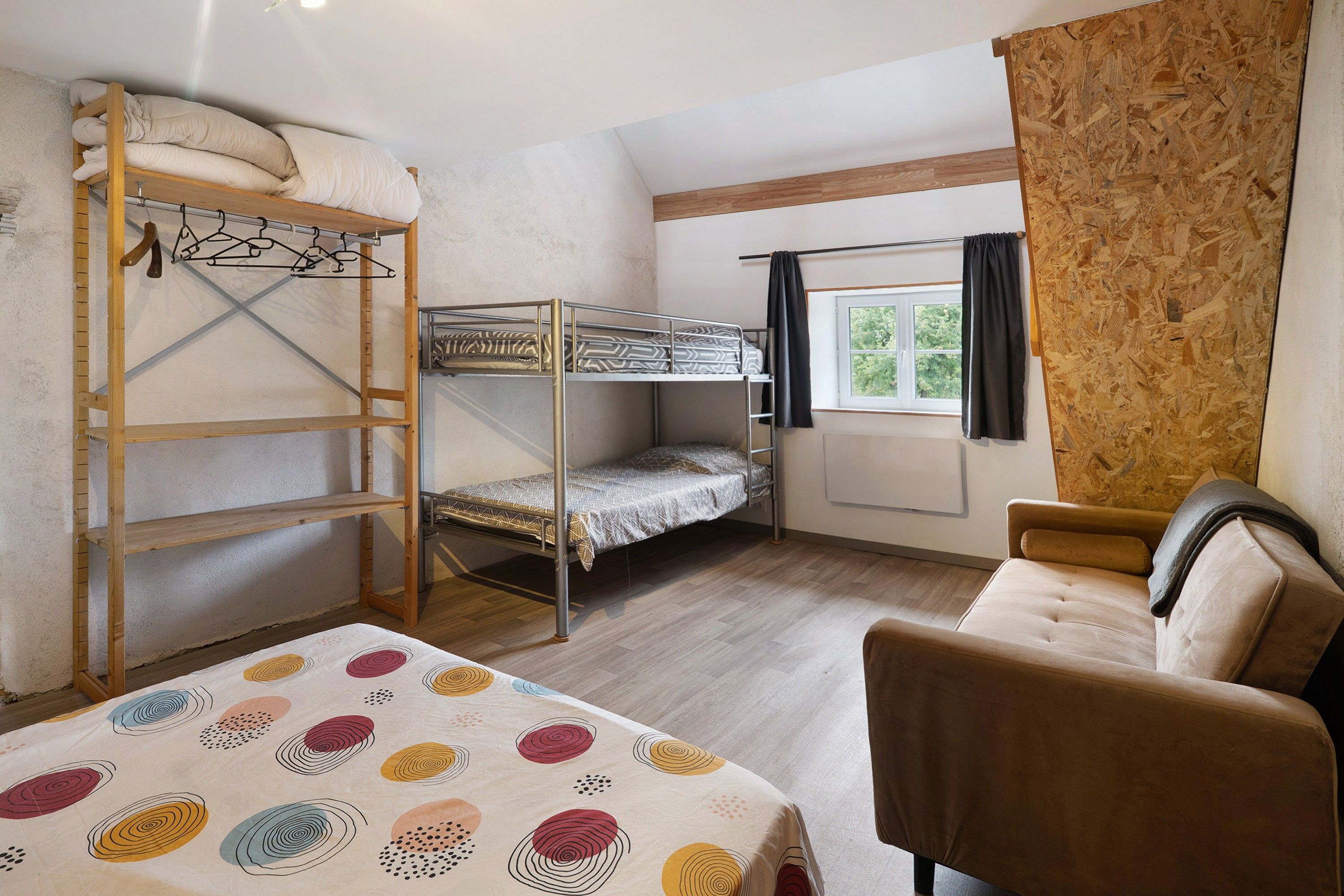 A dormitory room with bunk beds, a desk, a chair, and a window with curtains.