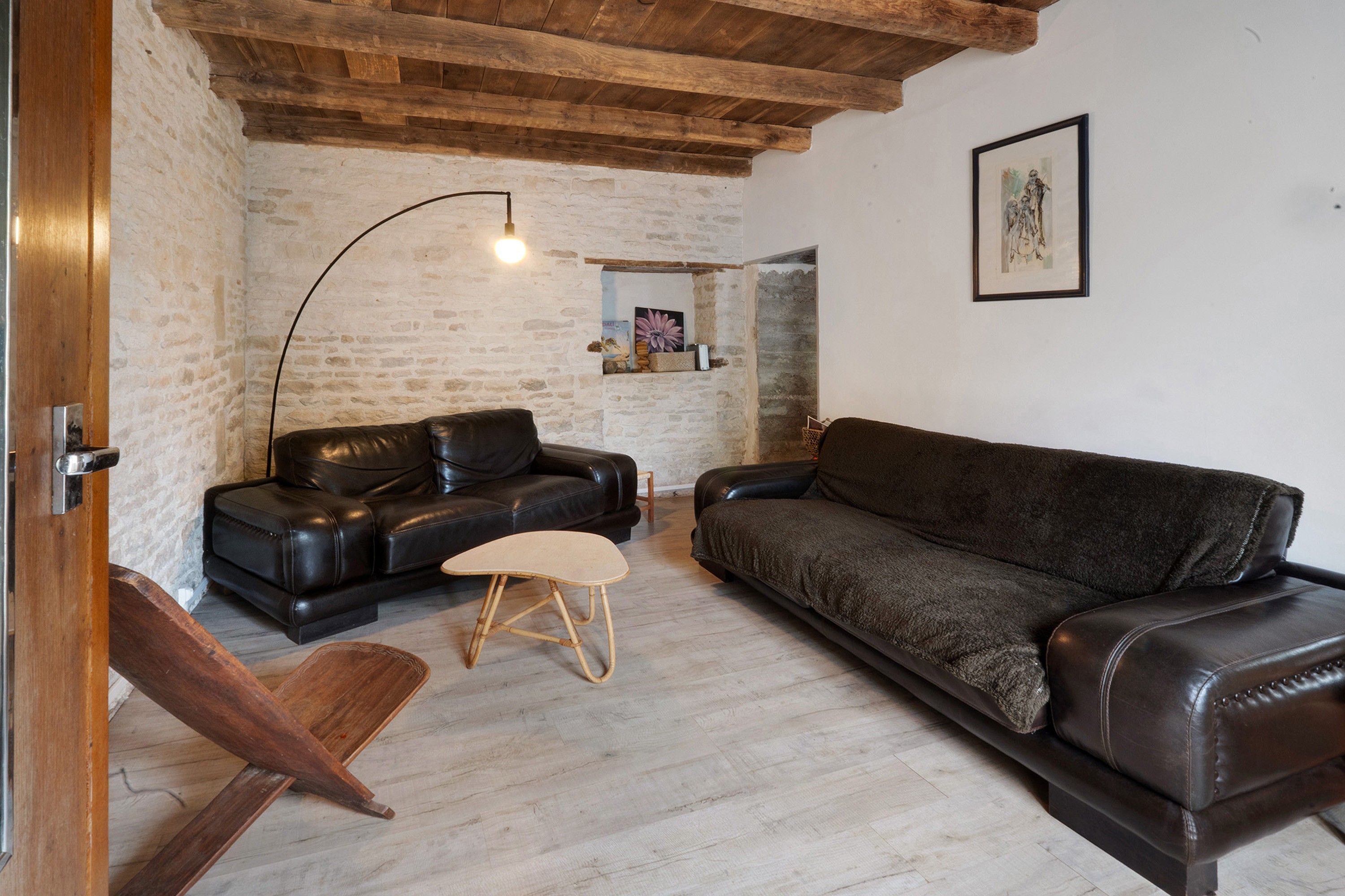 A living room with a black leather sofa, a wooden chair, a small stool, and a floor lamp.