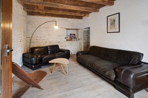 A living room with a black leather sofa, a wooden chair, a small stool, and a floor lamp.