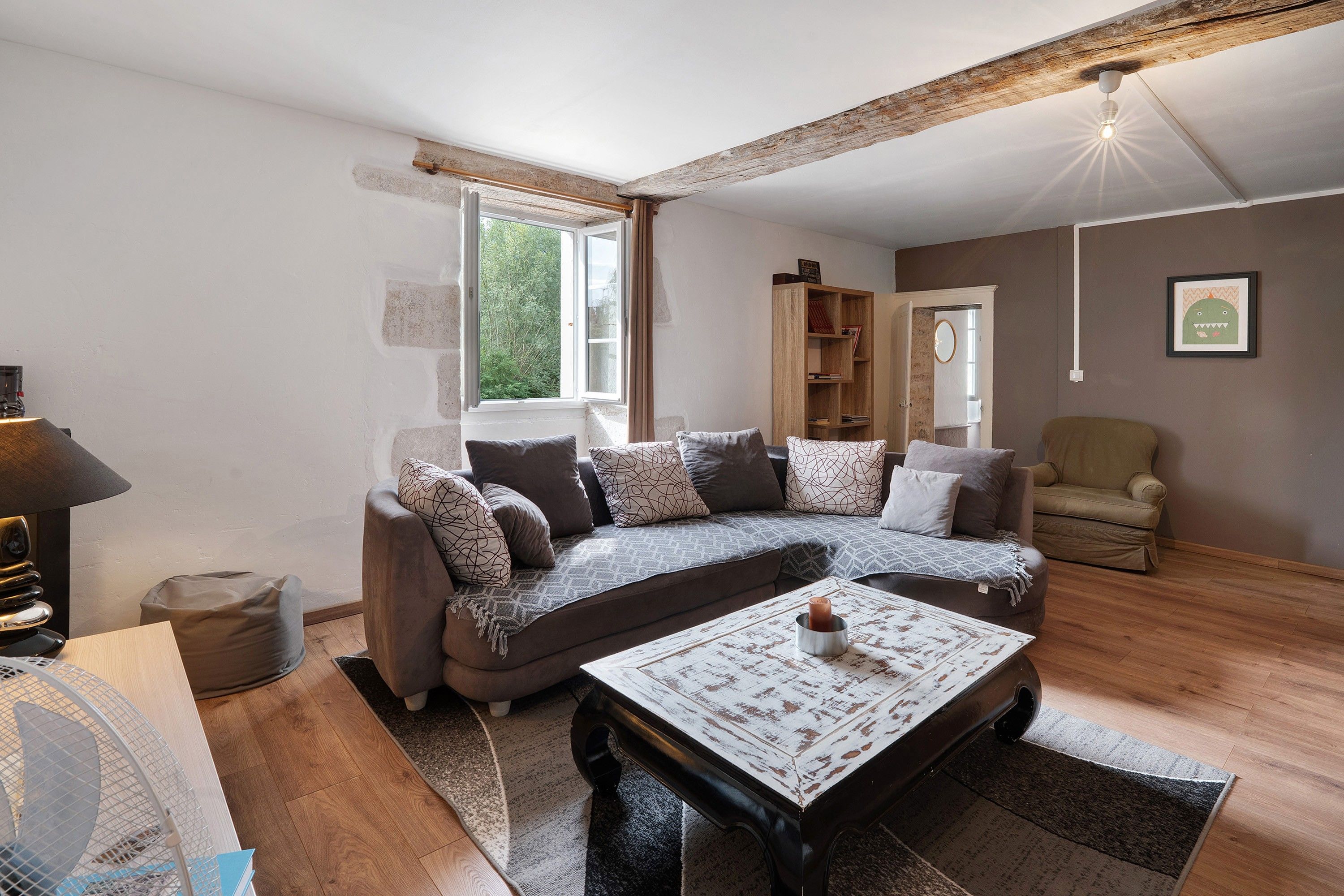 Ein Wohnzimmer mit einem Ecksofa, einem Couchtisch, einem Bücherregal und einem Sessel.