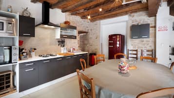 Une cuisine équipée d’appareils électroménagers modernes, une table à manger avec des chaises et un mur en pierre.