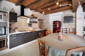 Une cuisine équipée d’appareils électroménagers modernes, une table à manger avec des chaises et un mur en pierre.